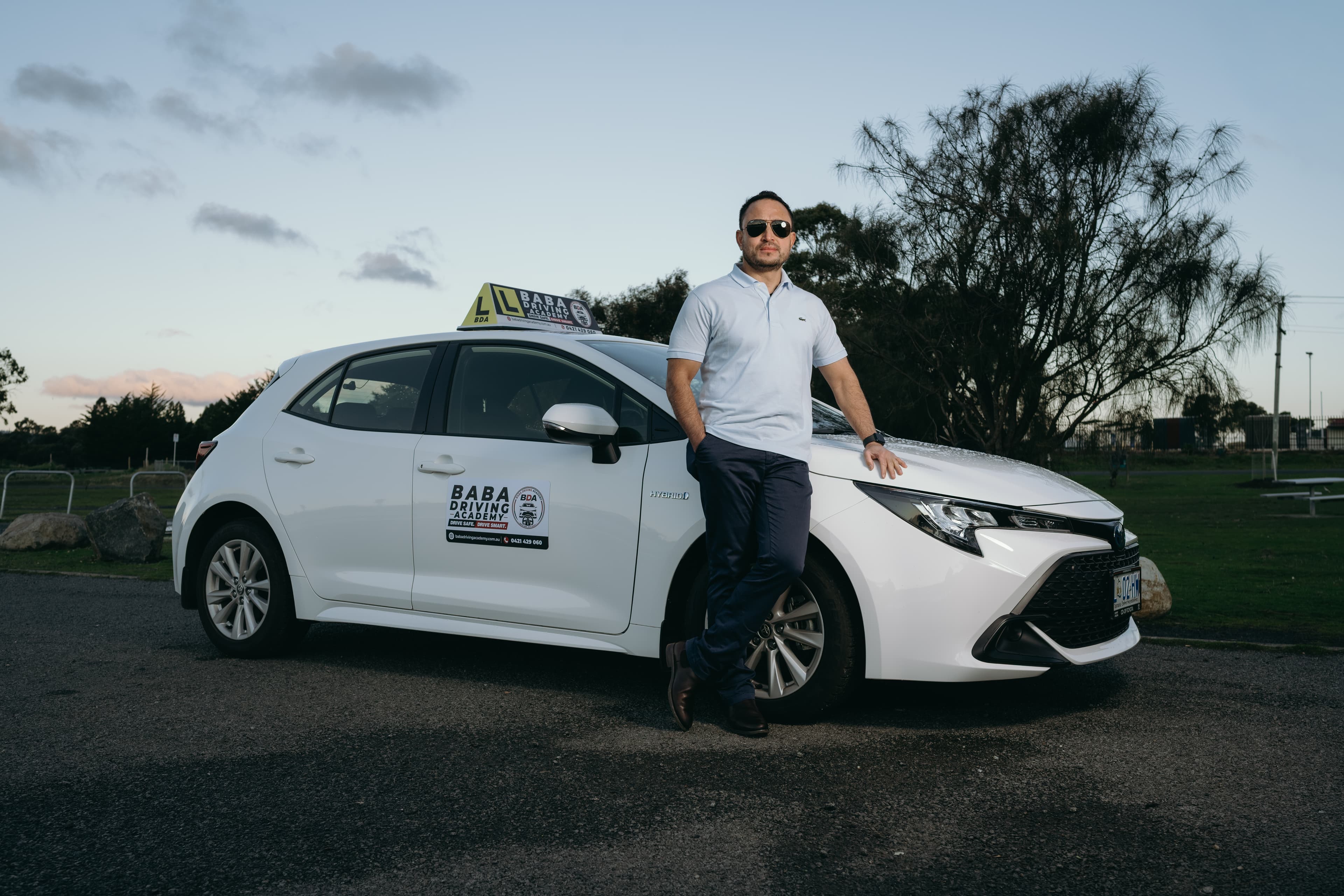 Indra Khadka, Australian Certified Driving Instructor at Baba Driving Academy, standing beside the dual-control automatic training car in Hobart, Tasmania.